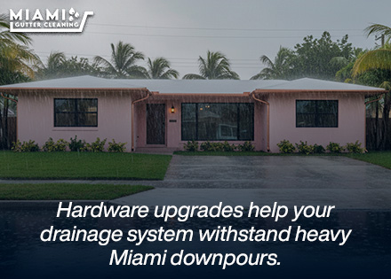 A wide shot of a multi-story Miami home during a heavy tropical rainstorm, showing clean water moving rapidly through reinforced channels and exiting downspouts smoothly.