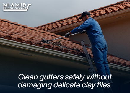 A uniformed technician from our maintenance division using soft-soled footwear and specialized flexible tools to clean gutters beneath curved barrel tile overhangs safely.
